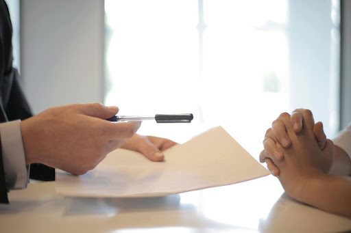 Person handing someone a document to sign with a pen